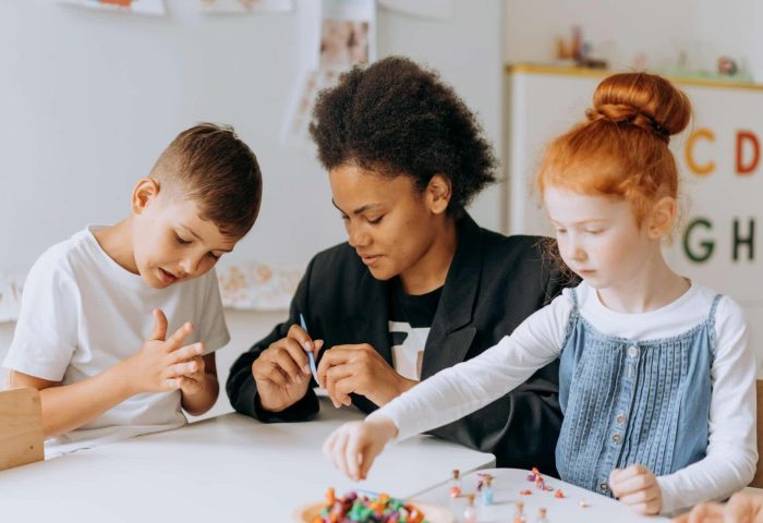A young black educator engaging in play based learning activity with two young children in a modern Australian classroom